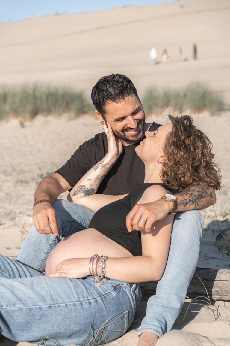 Couple enlacé qui se regarde dans les yeux en souriant lors de leur séance photo grossesse aux dunes du pilat