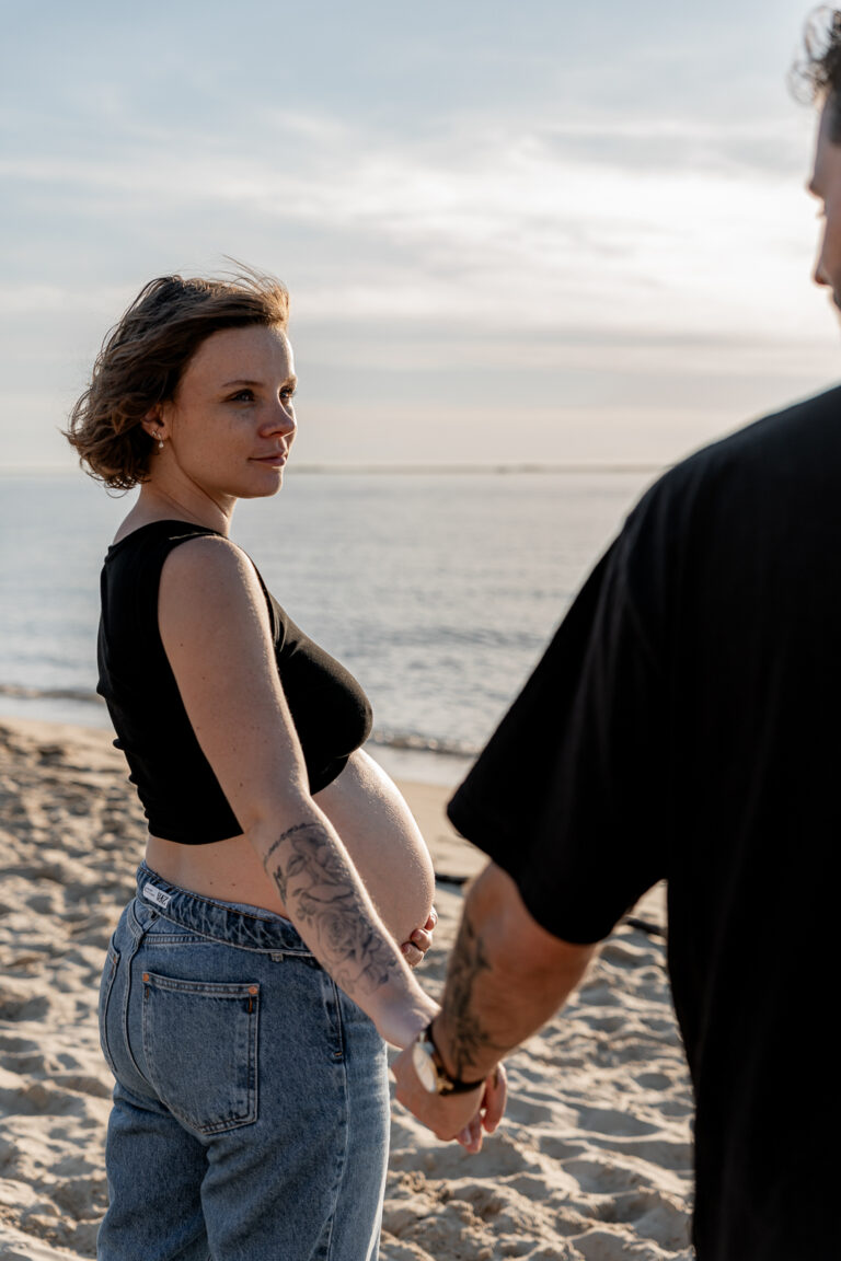 Future maman qui regarde le futur papa intensément, une main sous le ventre, devant la mer des dunes du pilat sur le bassin d'arcachon