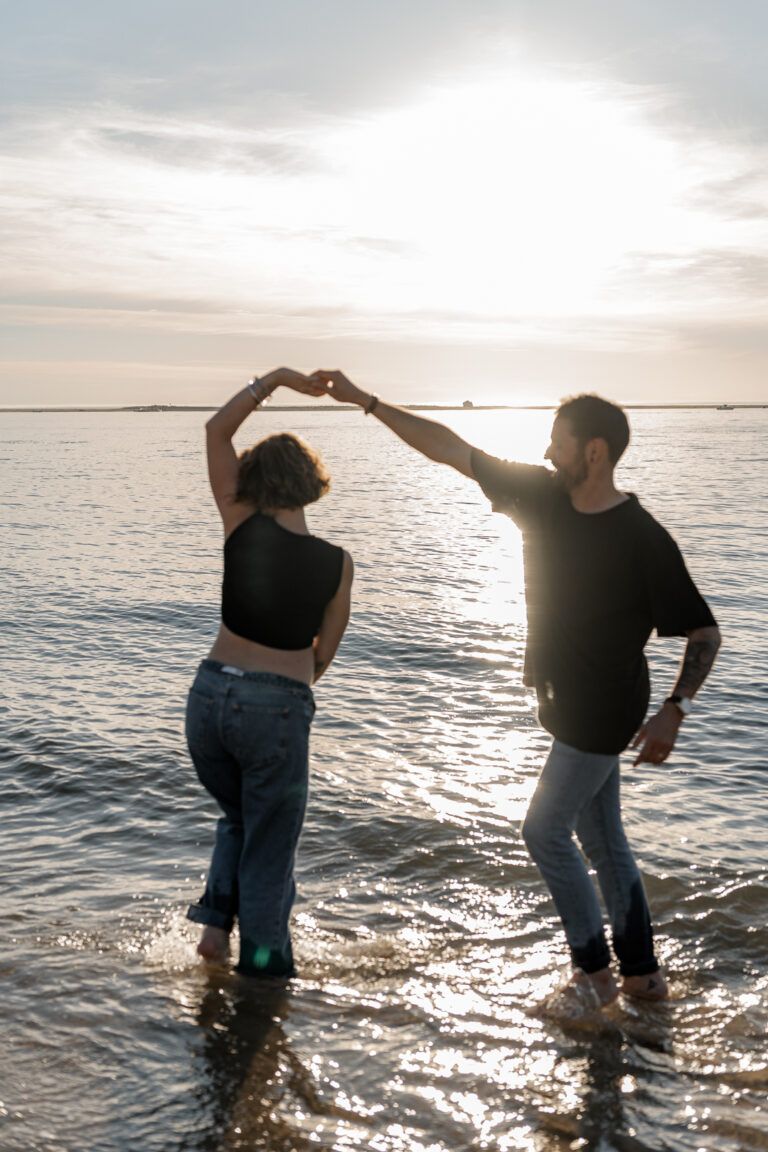 Couple qui danse les pieds dans l'eau sur la plage des Dunes du pilat sur le Bassin d'Arcachon lors de leur séance photo au coucher du soleil