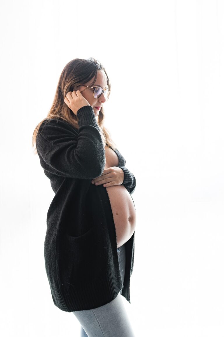 Photographe enceinte, dans un cardigan noir et un jean, qui met une mèche derrière son oreille