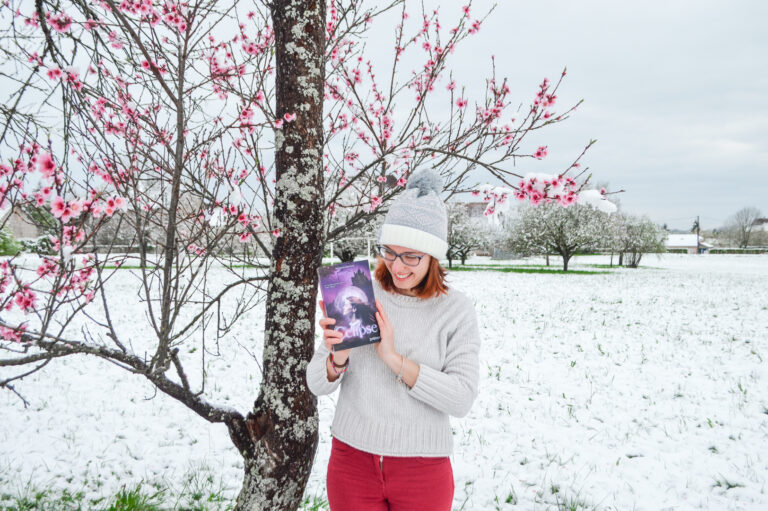 Photographe qui tient le livre qu'elle a écrit entre ses mains en souriant sous un manteau de neige et des fleurs de cerisiers