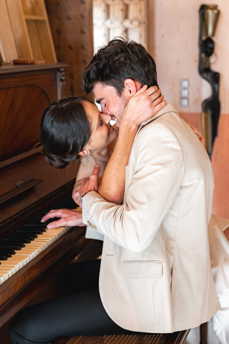 Mariés qui s'embrassent dans le salon d'un château de Saint-émilion devant un piano lors de la séance couple de leur mariage religieux à libourne