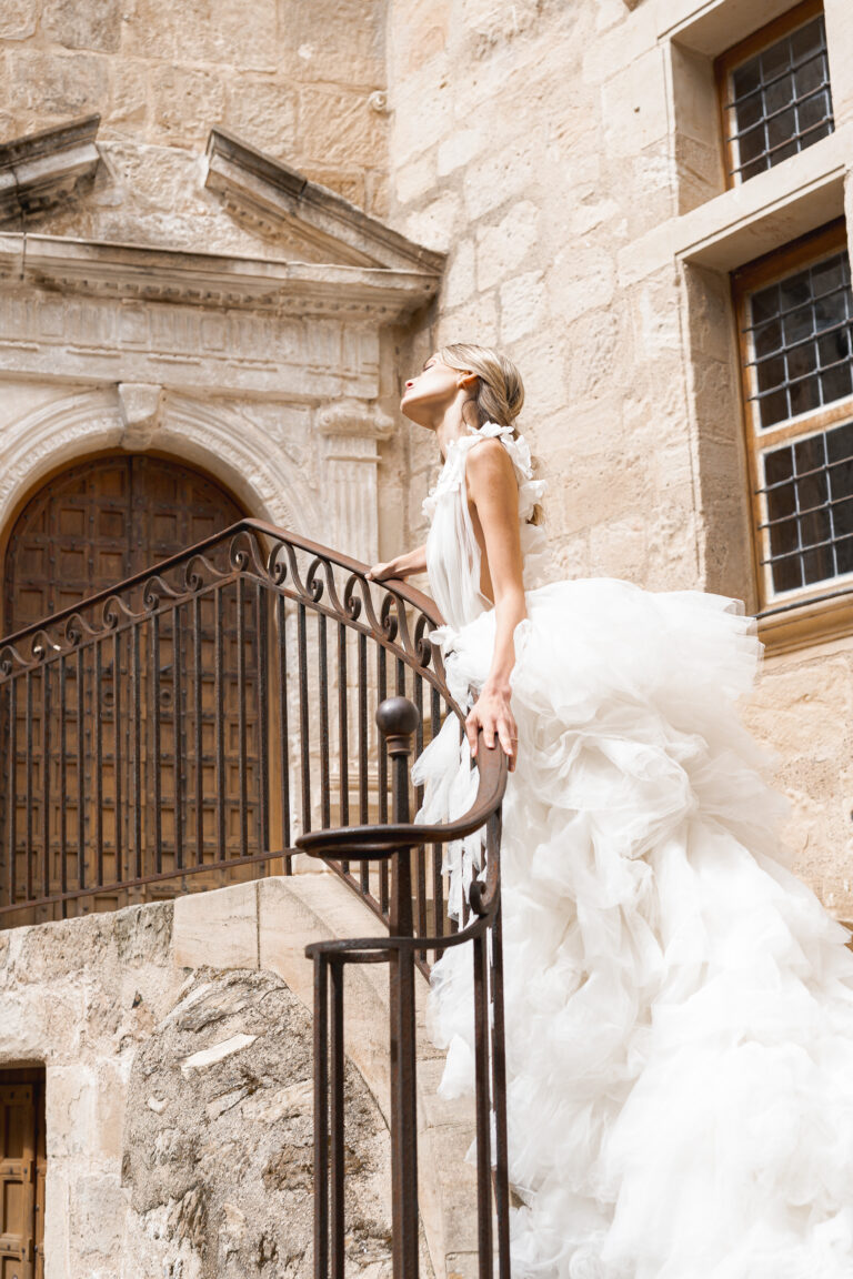 Mariée appuyée à une rambarde qui montre son cou gracieux dans une robe de créateur lors du portrait de la mariée de son mariage laïque dans un chateau de Saint-émilion