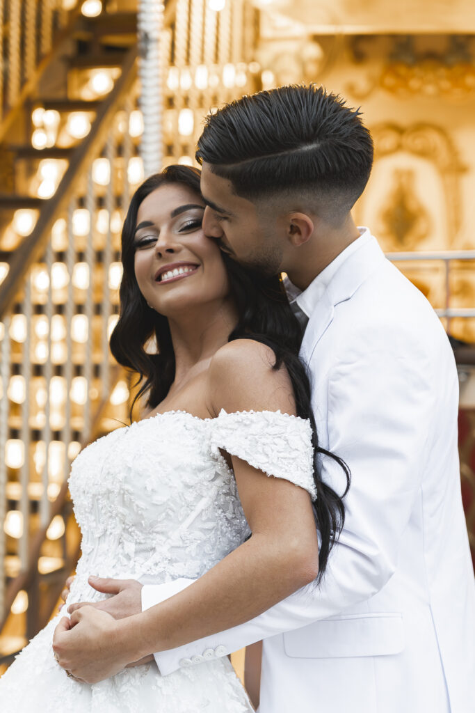 Marié qui embrasse la joue de sa femme devant le carrousel de l'avenue tourny lors de la séance couple de leur mariage à Bordeaux