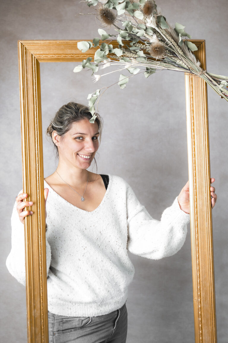 wedding designer et locatrice de mobilier qui tient un cadre fleuri en souriant lors d'une séance photo corporate à mon home studio à bordeaux